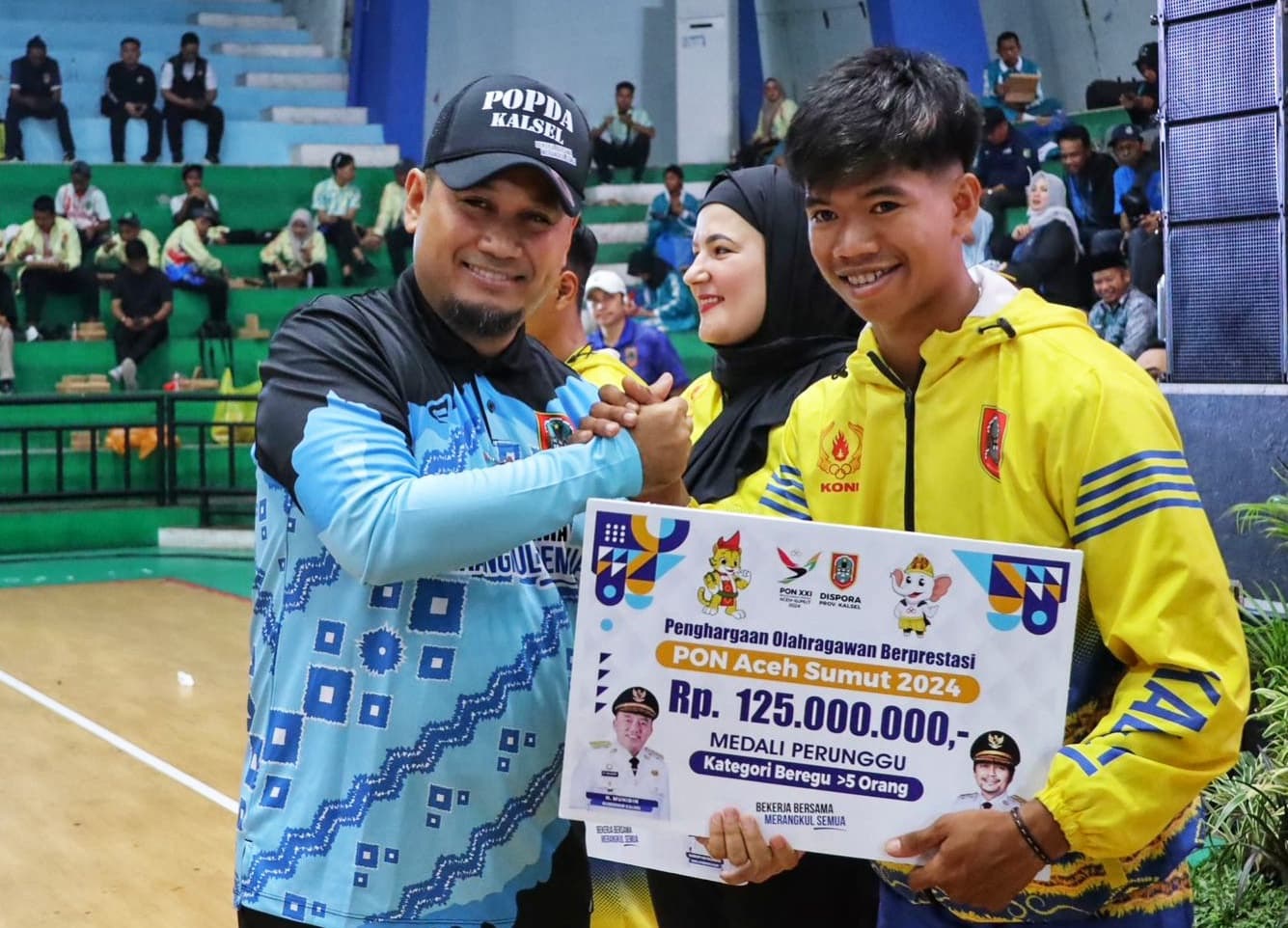 SIMBOLIS: Plt Kadispora Kalsel, Fitri Hernadi secara simbolis menyerahkan bonus kepada atlet peraih medali PON dan Peparnas 2024 saat pembukaan POPDA Kalsel 2025 di GOR Hasanuddin HM, Banjarmasin, Sen