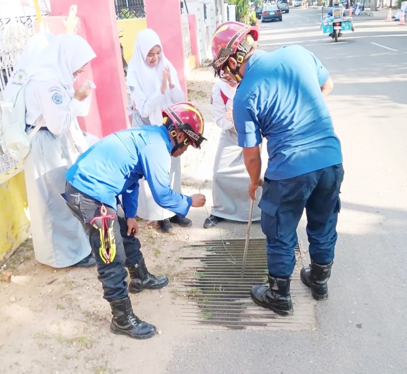 AMBIL KUNCI: Petugas Damkar Banjarbaru membantu pelajar mengambil kunci motor yang jatuh ke drainase di depan SMAN 2 Banjarbaru. (Damkar Banjarbaru Untuk Radar Banjarmasin).