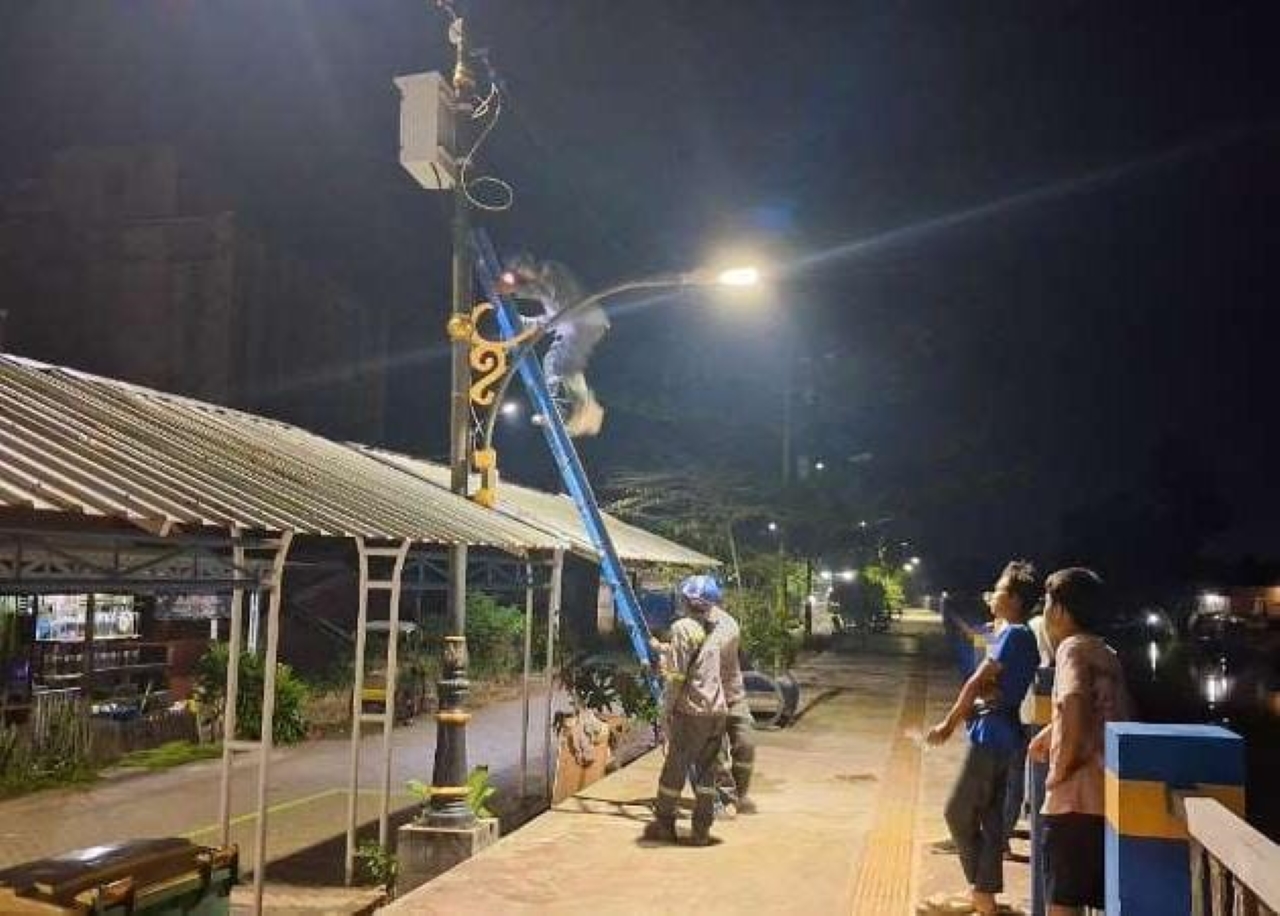 TERANG: Petugas DPRKPLH Banjar memperbaiki lampu PJU di Desa Murung Kenanga, salah satu jalur penting jemaah Haul Sekumpul.