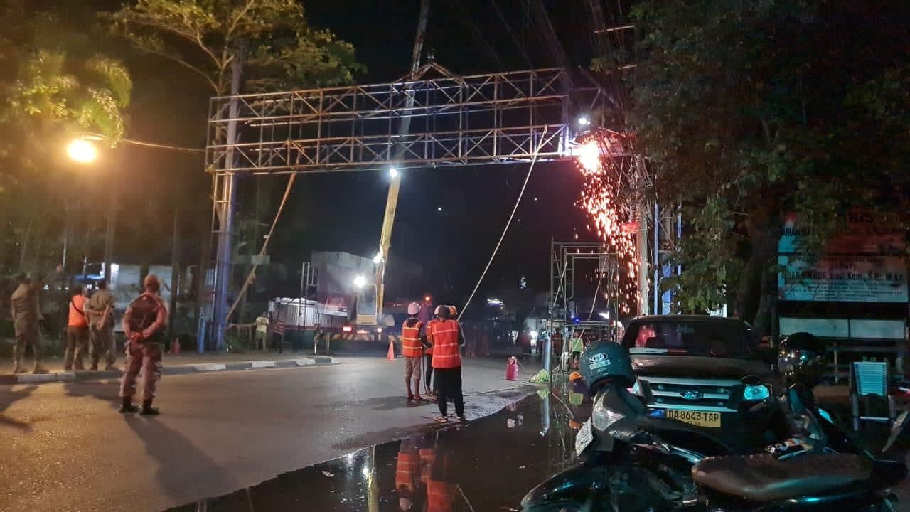 EKSEKUSI:Tim Satpol PP bersama teknisi akhirnya memotong rangka bando reklame di Jalan Sutoyo S, Sabtu (29/11/2025) dini hari lantaran pemilik mengabaikan tiga kali peringatan.