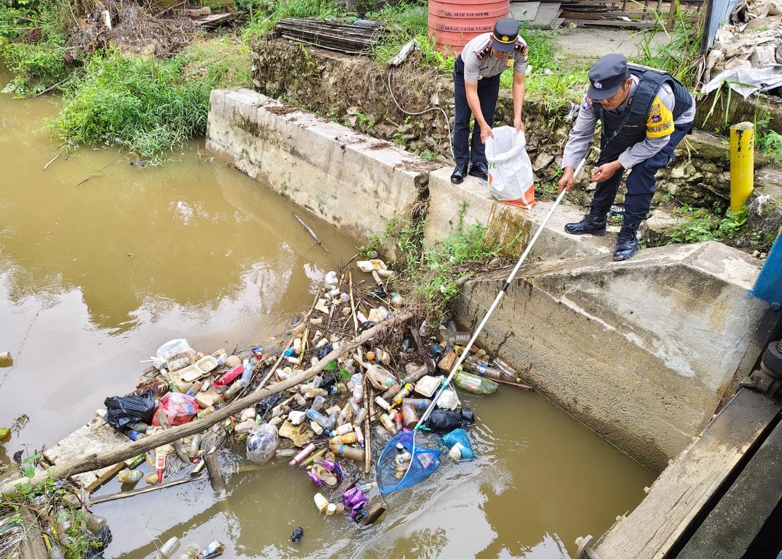 PEMANTAUAN: Dua personel Polsek Amuntai Utara melakukan pemantauan tinggi air di Pintu Air Sungai Turak Kecamatan Amuntai Utara, Kabupaten HSU, Selasa (9/12/2025).
