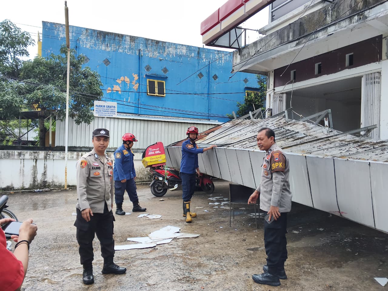 EVAKUASI: Petugas DPKP Kabupaten Banjar mengevakuasi kanopi Alfamart yang roboh dan menimpa sejumlah motor di Jalan A. Yani Km 12,9, Kecamatan Gambut, Minggu (21/12/2025) siang.