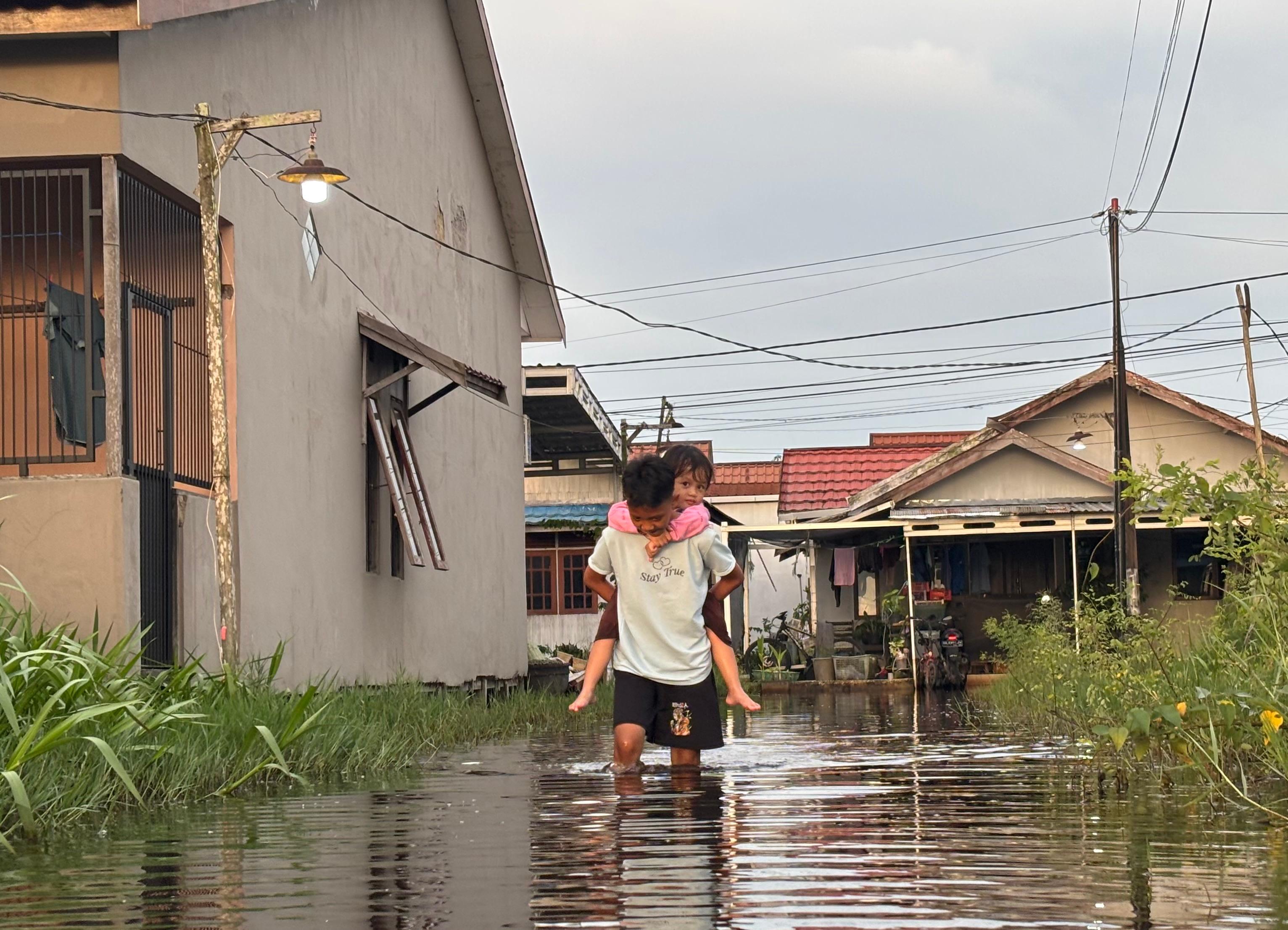 TEROBOS BANJIR: Tasya bersama adiknya menerobos banjir rob untuk bisa pulang pergi ke rumahnya di Pemurus Dalam, Banjarmasin Selatan.