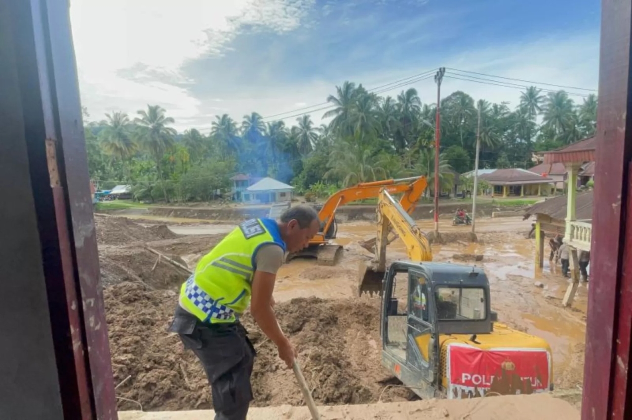 PEMULIHAN: Salah seorang personel kepolisian membantu membersihkan material lumpur di lokasi bencana di Sumatera. (Polri)