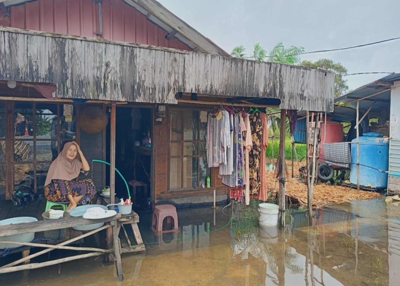TERENDAM: Mama Riani, salah satu korban banjir di Pengayuan duduk di teras rumahnya yang terendam, Senin (5/1).