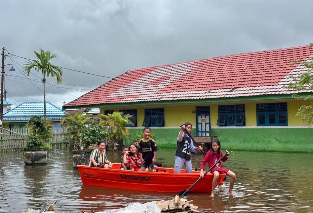 BANJIR: Sejumlah anak di Sungai Lulut Banjarmasin melintasi dalamnya banjir menggunakan perahu petugas.