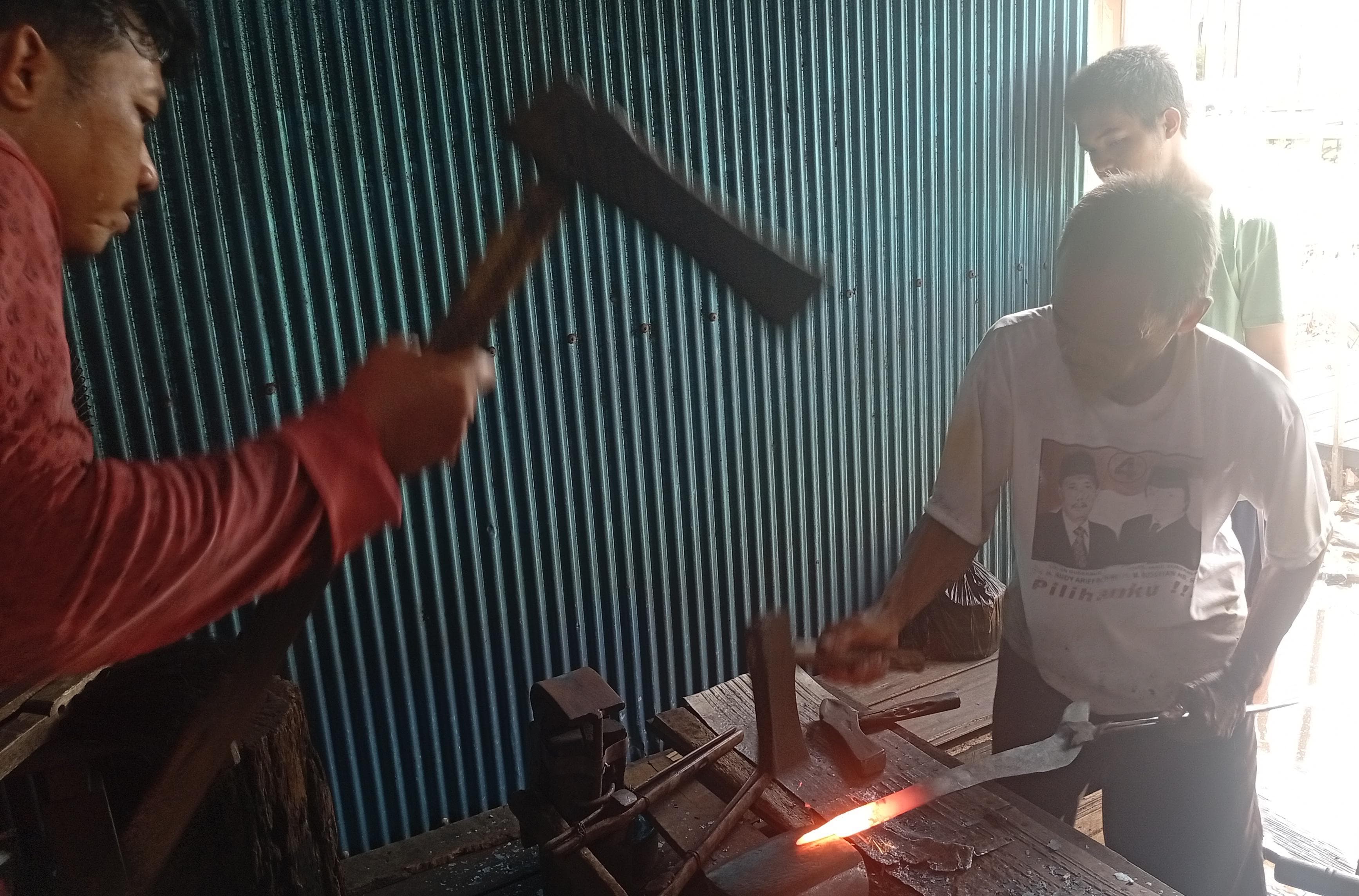 Pandai besi sedang menempa besi untuk membuat parang.