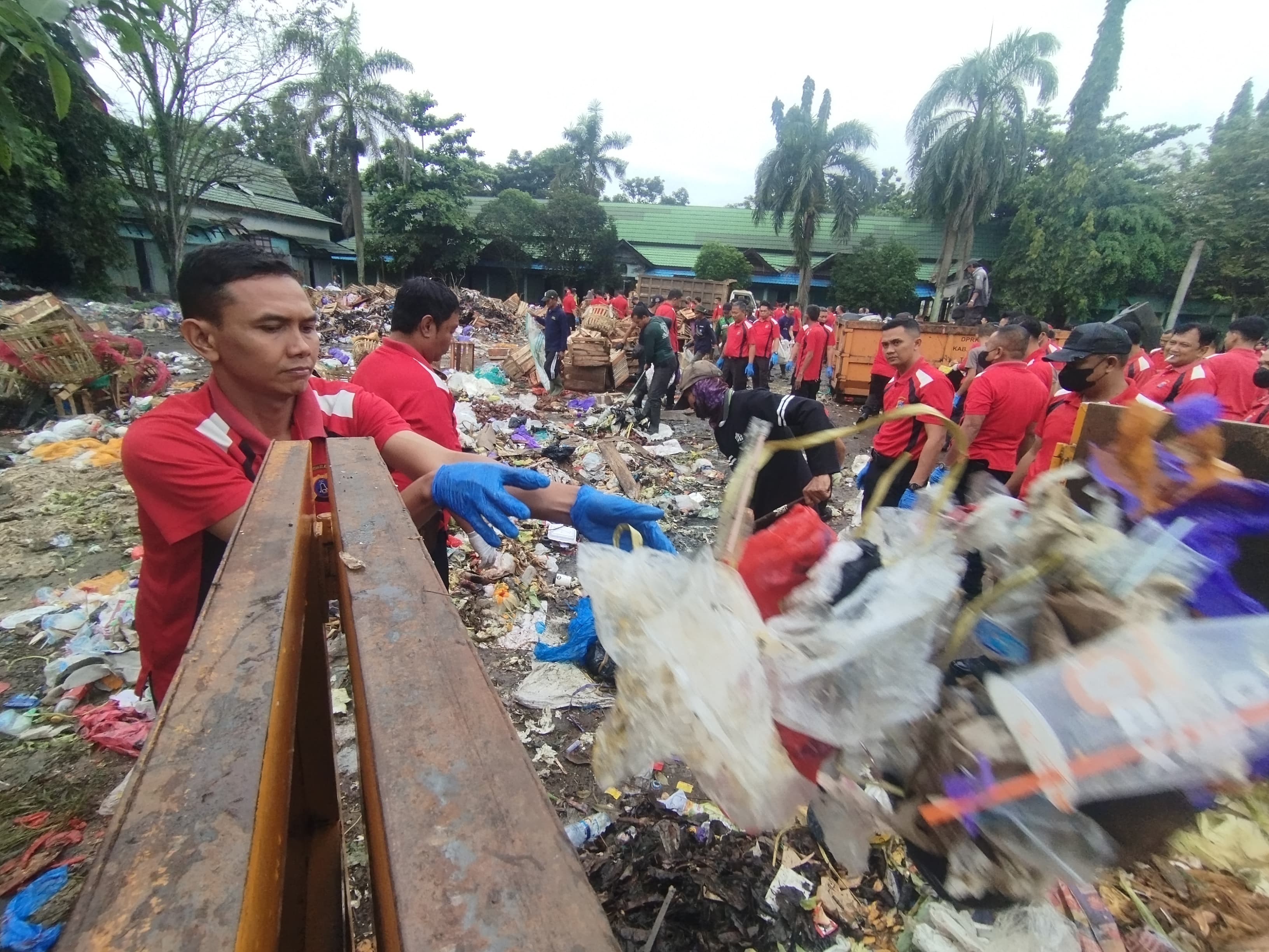 MENGANGKAT: Personel Polres Banjar mengangkat tumpukan sampah ke dalam bak kontainer saat aksi pembersihan di kawasan Pasar Pusat Perbelanjaan Sekumpul (PPS), Martapura, Jumat (6/2/2026).