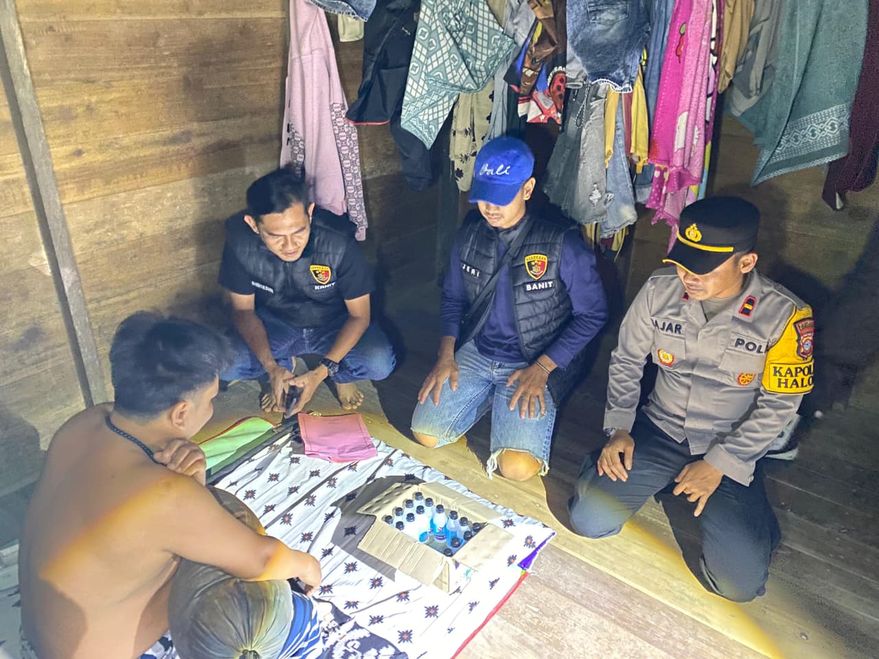 BAHAN GADUK: Kapolsek Halong Ipda Muhammad Fajar Saputra menunjukkan barang bukti 17 botol alkohol 95 persen yang disita dari kediaman warga dalam rangkaian Operasi Sikat Intan 2026.
