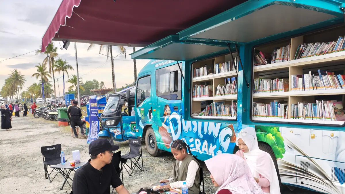 BACA BUKU: Pengunjung asal Angsana, Eka Sari, membaca buku bersama keluarga di pojok baca perpustakaan keliling pada Expo Tanah Bumbu 2026. (Foto: Zulqarnain/Radar Banjarmasin)&nbsp;