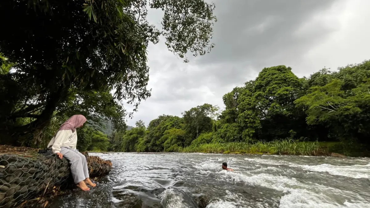 Seorang pengunjung duduk di tepian sungai, sementara lainnya berenang di arus deras Sungai Nateh, Sabtu (4/4/2026). Jamaluddin/Radar Banjarmasin.