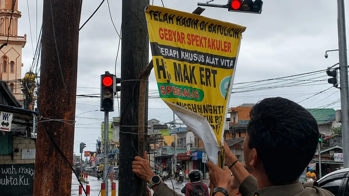 PENERTIBAN: Petugas Satpol PP Tanah Bumbu menurunkan reklame liar yang dipasang di fasilitas umum di kawasan Simpang Empat.