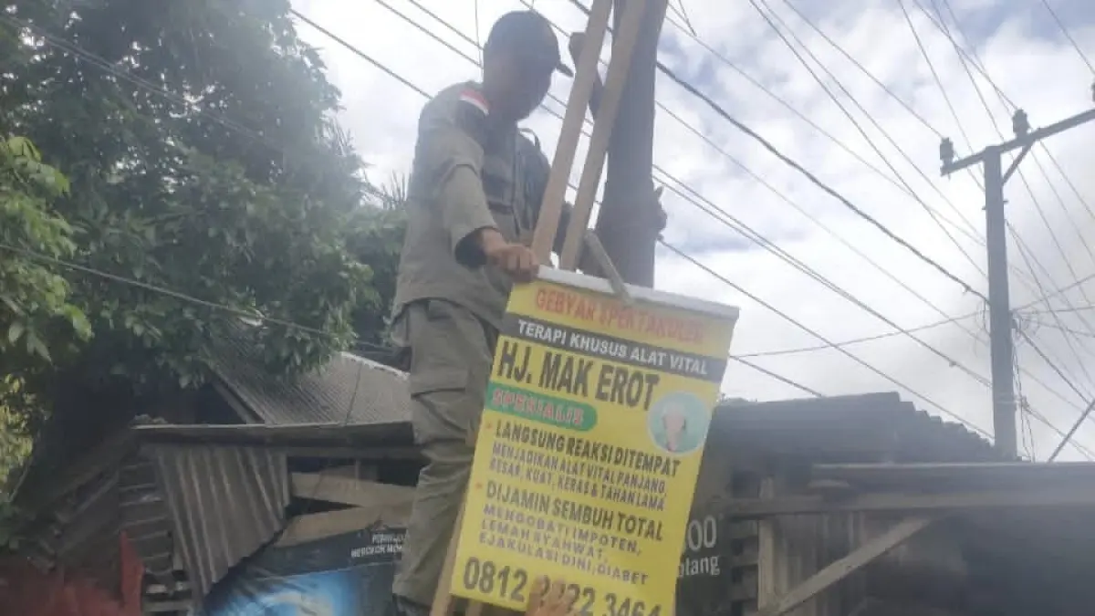 PENERTIBAN: Petugas Satpol PP dan Damkar Tanah Bumbu menurunkan papan iklan yang dipasang di tiang fasilitas umum saat patroli ketertiban di wilayah Simpang Empat. (Foto: Satpol PP untuk Radar Banjarmasin)