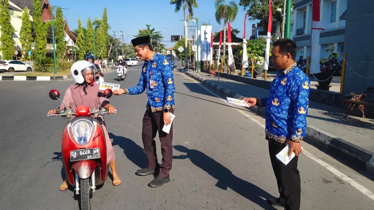 SOSIALISASI: Kepala Badan Pendapatan Daerah (Bapenda) Budia Hendra Kabupaten Hulu Sungai Utara membagikan brosur sosialisasi Program Berburu Struk Tapping Box kepada pengendara di kawasan Bundaran Salawat Amuntai. (Foto: M Akbar/Radar Banjarmasin)