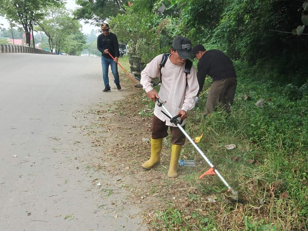 DIBERSIHKAN: Pembersihan pinggir Jalan KH Harun Nafsi yang dipenuhi rumput liar dilakukan tim kecamatan.