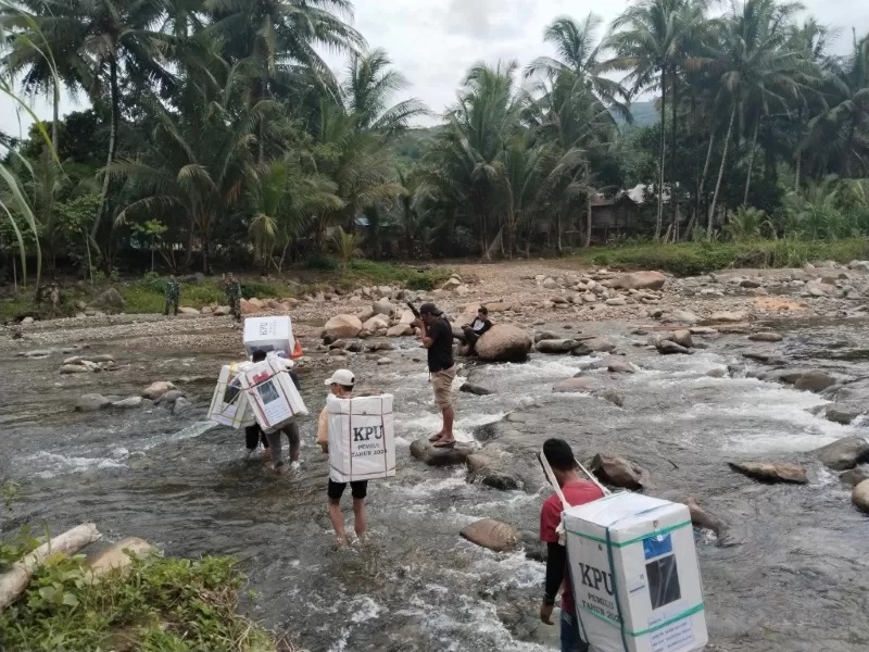 MENYEBERANG SUNGAI: Porter melewati Sungai Batang Alai Timur membawa logistik Pemilu 2024 ke dua desa yang sulit dijangkau di Pegunungan Meratus. ( FOTO: KPU HST untuk RADAR BANJARMASIN.)