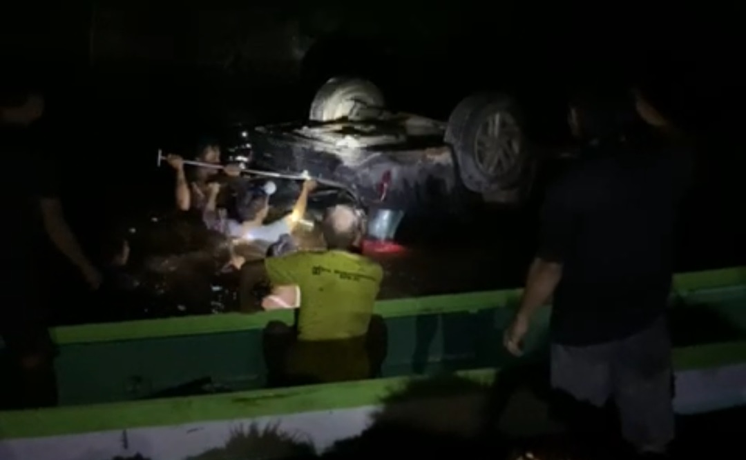TERCEBUR SUNGAI: Warga menolong sopir dan penumpang di dalam mobil yang terbalik di tikungan SMK Negeri 4, Jalan Pangkalan Bun menuju Kotawaringin Lama, Kelurahan Mendawai Seberang, Minggu (18/2/2024)