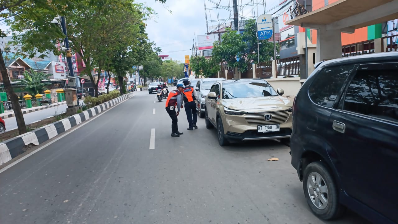 TEGAS: Tim Dishub menggemboskan ban mobil yang parkir di tepi jalan sebagai bentuk tindakan tegas.