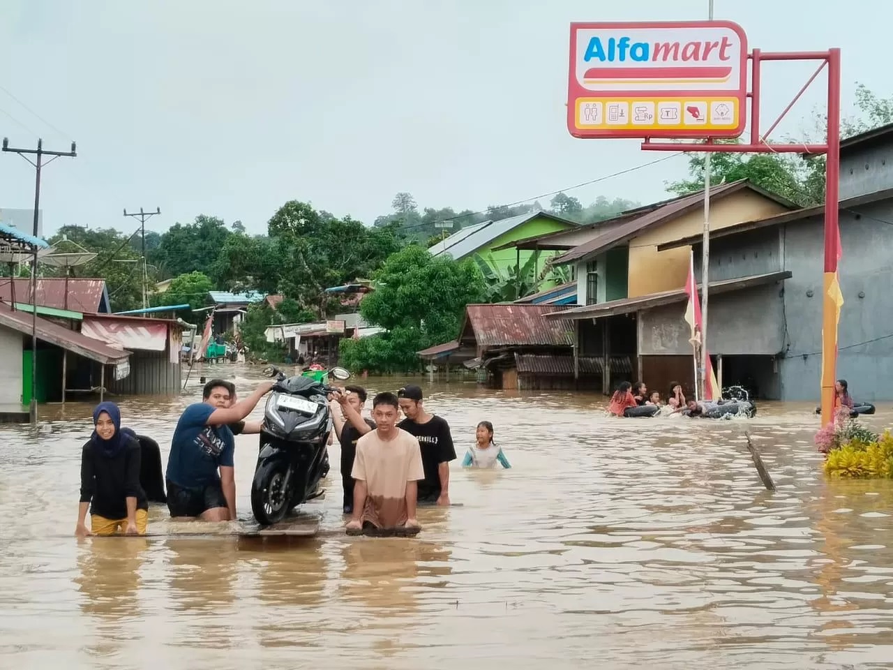Warga menggotong sepeda motor menyeberangi banjir di Desa Serimbu Kecamatan Air Besar Kabupaten Landak pada Rabu (22/5). (ISTIMEWA)