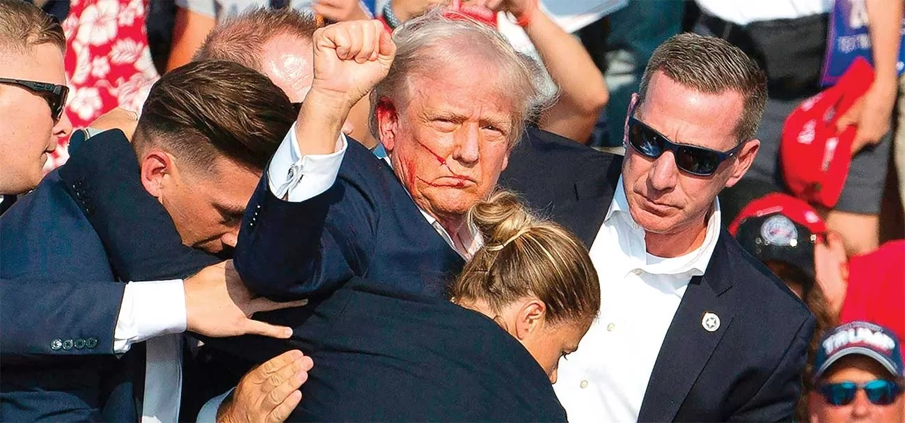 DARAH DI WAJAH KANDIDAT: Donald Trump dikelilingi petugas Secret Service dan dibawa turun dari panggung kampanye di Butler, Pennsylvania (13/7). (REBECCA DROKE/AFP)