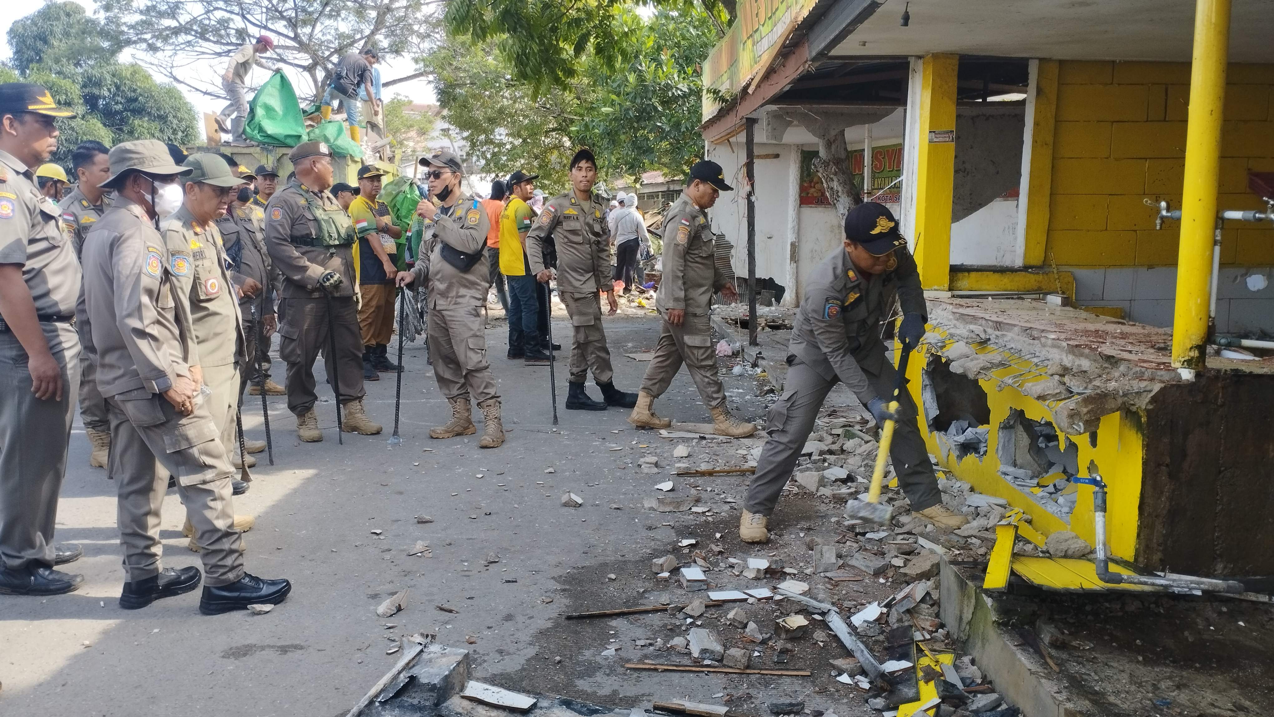 TEGAS: Tim Satpol PP membongkar lapak pedagang di tepi Jalan Sultan Hasanuddin Kecamatan Samarinda Seberang dan kecamatan Loa Janan Ilir, Selasa (16/7). Foto lain, tim DLH berupaya mengambil sisa mate