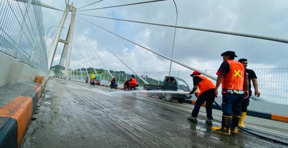 CEGAH MUSIBAH: Tim Disdamkar dan Penyelamatan Samarinda membersihkan sisa kerikil dari aspal yang dikupas imbas proyek peningkatan jalan di Jembatan Achmad Amins, Minggu (21/7). (FOTO: RAMA/KP)