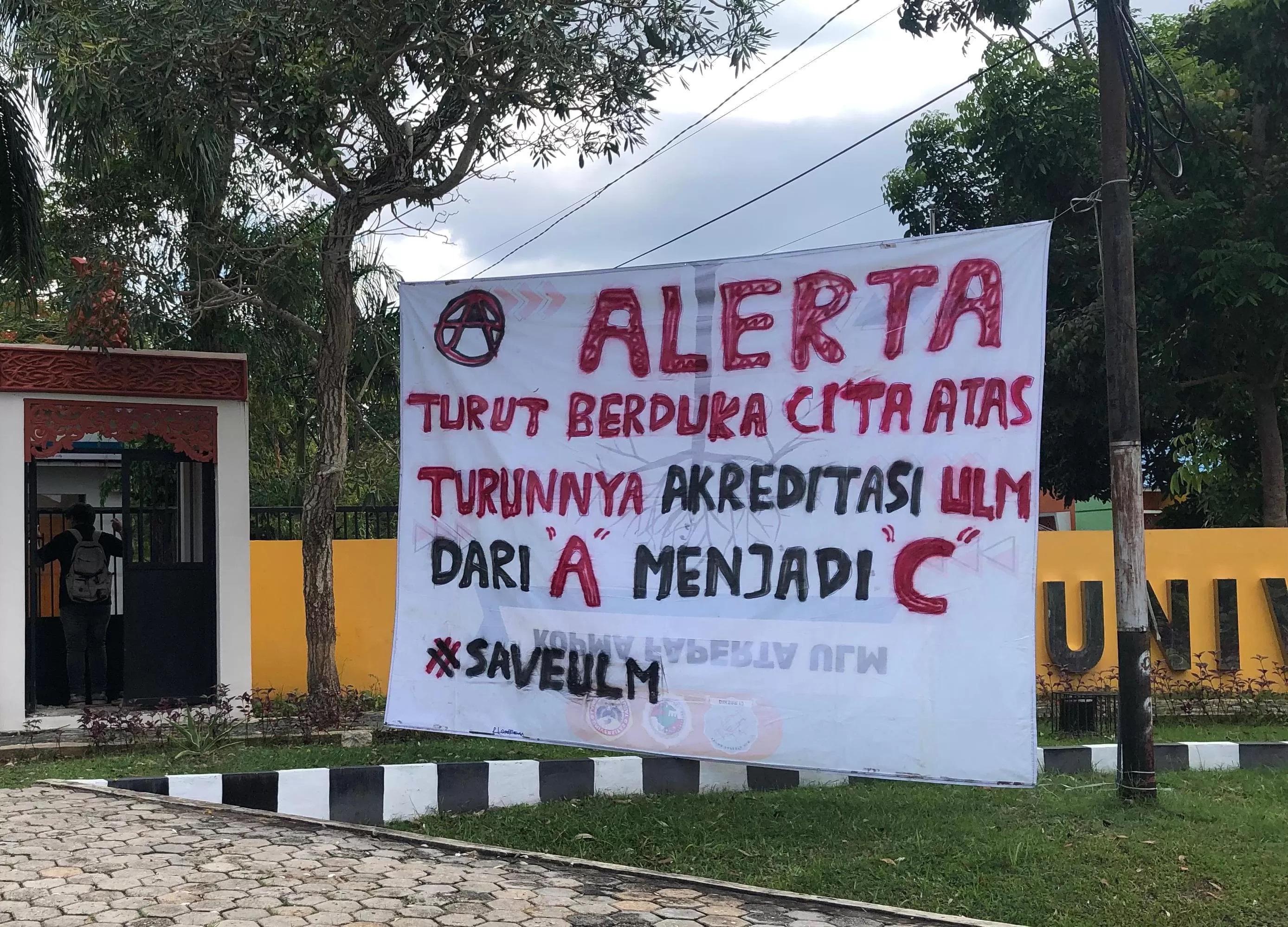 SAVE ULM:Mahasiswa memasang spanduk turut berduka cita atas turunnya akreditas ULM dari A ke C di dekat gerbang Kampus ULM Banjarbaru.(foto:Sheilla Farazela/Radar Banjarmasin)
