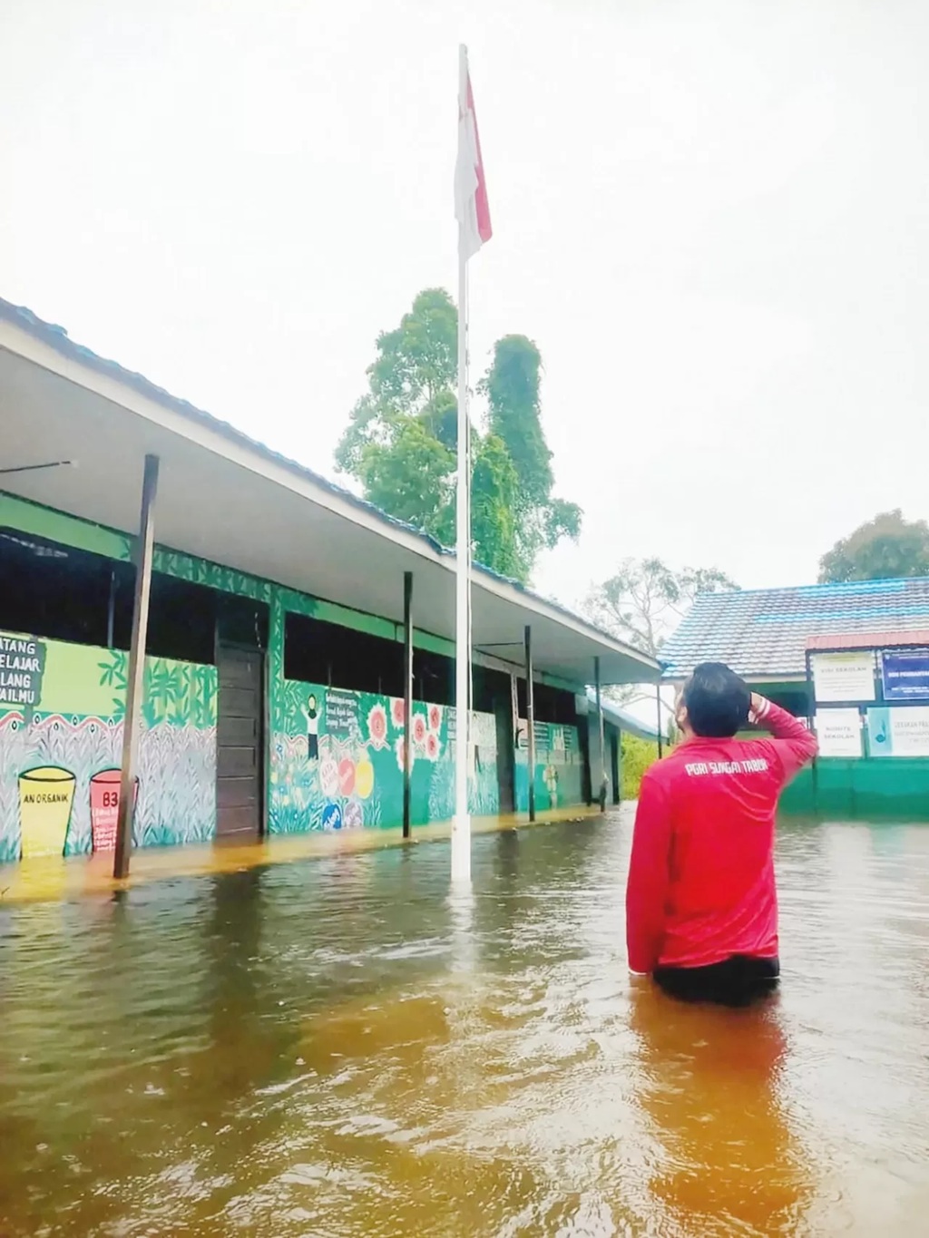 HORMAT: Salah satu guru di SDN Pembantanan 1 hormat ke bendera saat sekolahnya kebanjiran. Tahun ini Disdik Banjar memprioritaskan memperbaiki sekolah yang terdampak banjir. (SDN PEMBANTANAN 1)
