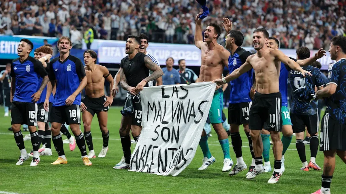 Pemain Argentina membawa spanduk bertuliskan Malvinas milik Argentina. Inggris dan Argentina pernah berperang memperebutkan Malvinas.