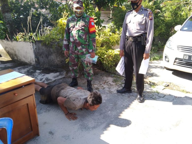 JALANI SANKSI: Seorang warga dihukum push up karena tak menggunakan masker saat operasi yustisi di depan Mako polsek Mandor, Minggu (25/7).