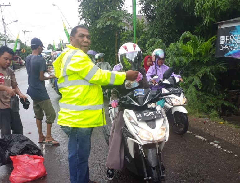 MOMEN: Koordinator Relawan Rest Area Masjid Baitul Kiram, Juniansyah hujan-hujan membagikan bingkisan kepada pengendara menuju haul Guru Sekumpul. | Foto: Ist untuk Radar Banjarmasin