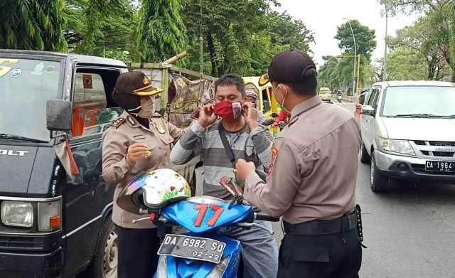 DIPASANGKAN: Polisi memasangkan masker kepada pengendara motor di perempatan Jalan Merdeka, Banjarmasin Tengah, Selasa (14/4) pagi.