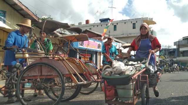 CARI NAFKAH: Seorang ibu berkeliling kota menjaja ikan melewati para tukang becak yang belum dapat penumpang. Penghasilan mereka sekarang jauh menurun karena wabah corona.