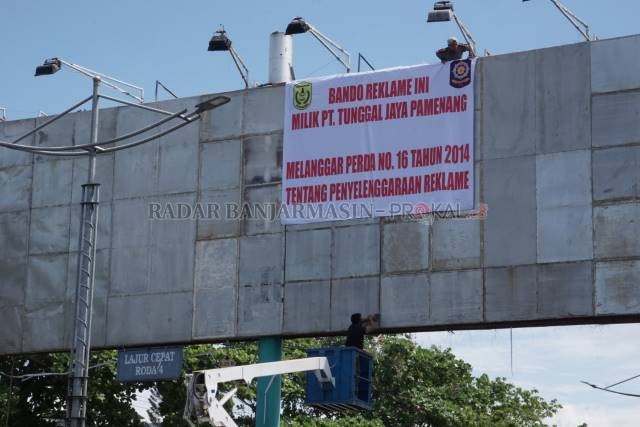 PERINGATAN: Personel Satpol PP memasang spanduk peringatan di atas baliho bando yang izinnya tak lagi diperpanjang pemko. | FOTO: WAHYU RAMADHAN/RADAR BANJARMASIN