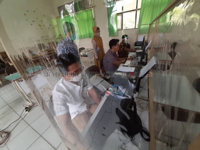 TIRAI PELINDUNG: Ruang kerja untuk mengakses PPDB di SMPN 7 Banjarmasin menerapkan protokol COVID-19. Tampak petugas meng-input data calon siswa. | FOTO: WAHYU RAMADHAN/RADAR BANJARMASIN