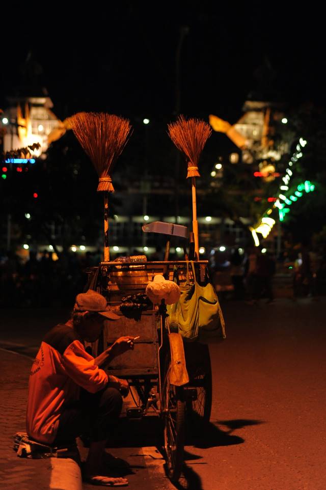 REHAT SEJENAK: Penyapu jalan duduk melepas lelah di samping gerobak peralatannya. Dipotret di Jalan Sudirman beberapa waktu lalu. | FOTO: DOKUMEN RADAR BANJARMASIN