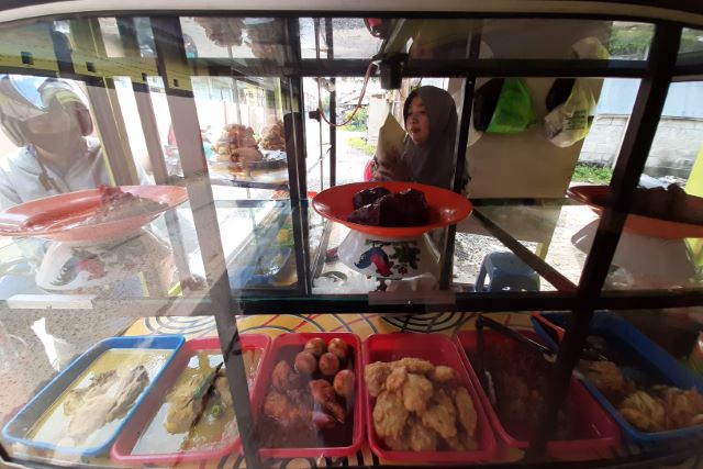 SEPI PEMBELI: Hj Midah membungkus nasi campur yang dipesan pembeli. Sejak pandemi melanda Banjarmasin, pedagang nasi di sepanjang Jalan Cendana kepayahan. | FOTO: WAHYU RAMADHAN/RADAR BANJARMASIN