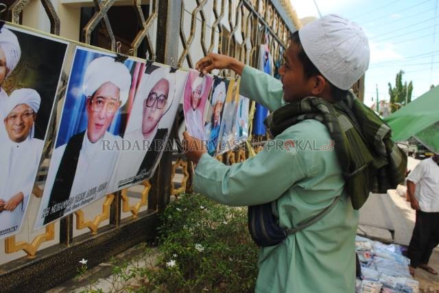 BAKAL DIBENAHI: Seorang pedagang saat menata dagangannya berupa poster para ulama di pagar Masjid Pancasila, Martapura saat Haul ke-15 Guru Sekumpul awal 2020. | FOTO: DOK RADAR BANJARMASIN