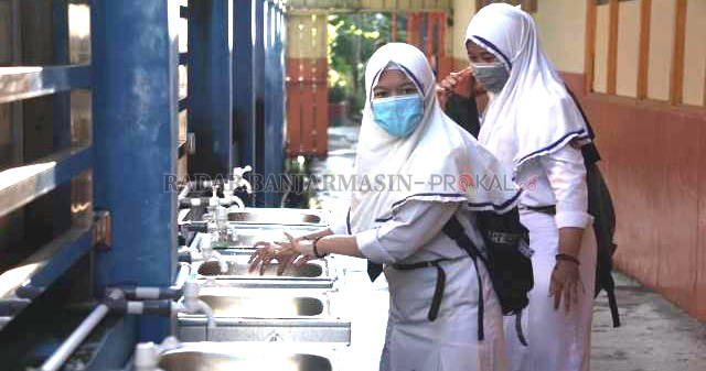 SIMULASI: Siswi SMPN 10 Banjarmasin di Jalan AES Nasution mencuci tangan sebelum memasuki kelas. Foto diambil pada awal simulasi kemarin. | FOTO: WAHYU RAMADHAN/RADAR BANJARMASIN