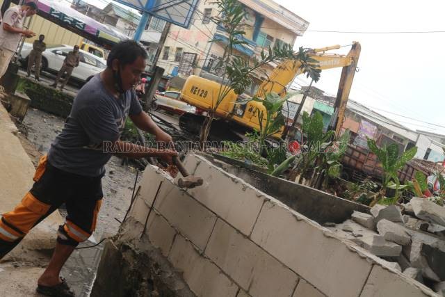 DIGODAM: Warga membongkar tembok pemisah ruko untuk membuat jalan alternatif. Tampak dalam latar foto, alat berat sedang mengeruk Sungai Veteran. | FOTO: TIA LALITA NOVITRI/RADAR BANJARMASIN