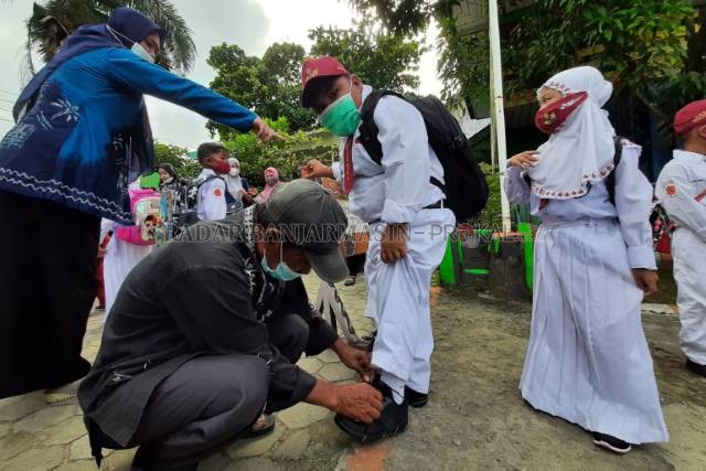 MASKERNYA MANA: Staf keamanan sekolah membenarkan tali sepatu siswa SDN Karang Mekar 5. | FOTO: WAHYU RAMADHAN/RADAR BANJARMASIN