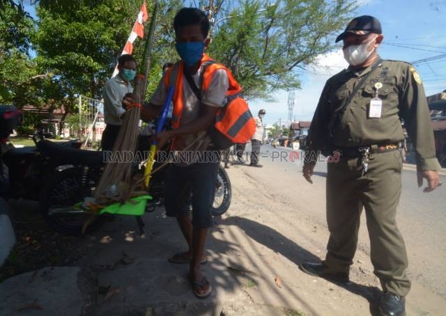SANKSI SOSIAL: Warga kota yang terjaring tak memakai masker selama PPKM dihukum Satpol PP dengan menyapu jalan. | FOTO: WAHYU RAMADHAN/RADAR BANJARMASIN