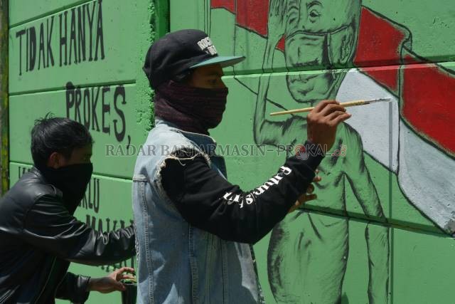KEBEBASAN BEREKSPRESI: Dua seniman tato asal Banjarmasin, A dan B melukis mural di tembok eks Pelabuhan Marla, Jalan RE Martadinata, kemarin (29/8). Aksi mereka didukung warga sekitar dan pengendara yang melintas. | FOTO: WAHYU RAMADHAN/RADAR BANJARMASIN