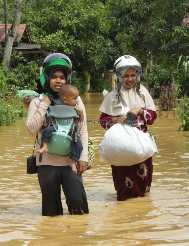 MENGUNGSI: Warga Jalan Telaga Padawangan membawa anaknya menuju dataran tinggi. Rumah mereka terendam hingga ketinggian 50 cm, Selasa (16/11) . \ Foto: JAMALUDDIN/RADAR BANJARMASIN