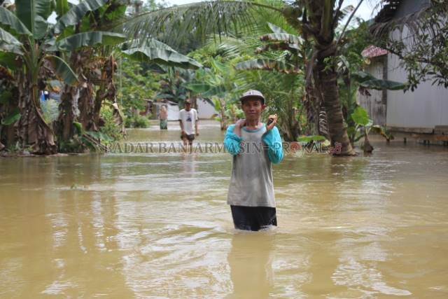 TERJANG BANJIR: Warga Desa Masiraan, Kecamatan Pandawan menerjang banjir melintasi jalan desa. | FOTO: JAMALUDDIN/RADAR BANJARMASIN