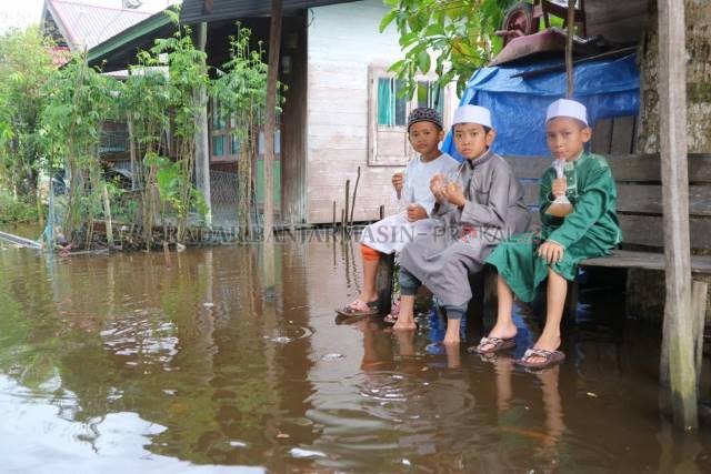 BANJIR ROB: Sambil makan dan minum anak-anak d Kecamatan Candi Laras Selatan duduk santai di tengah genangan air. Banjir rob melanda Kecamatan Candi Laras Selatan dan Kecamatan Candi Laras Utara, Kabupaten Tapin. | Foto: Rasidi Fadli/Radar Banjarmasin