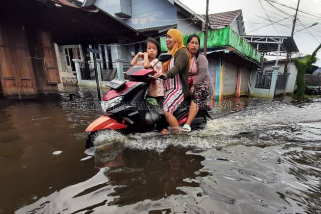 TEROBOS BANJIR: Warga Jalan Prona di Banjarmasin Selatan, menerobos banjir yang merendam jalan dan permukiman. | FOTO: WAHYU RAMADHAN/RADAR BANJARMASIN