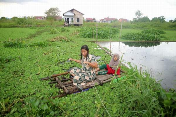 TEROBOS RAWA: Menggunakan rakit seadanya jadi satu-satunya cara yang digunakan Halimah dan keluarganya untuk bisa sampai ke jalan. | FOTO: WAHYU RAMADHAN/RADAR BANJARMASIN