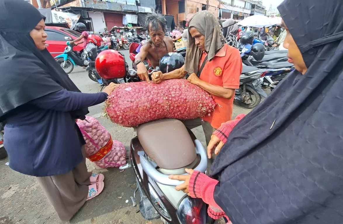 ATUR POSISI: Pembeli menaikkan karung berisi bawang merah ke atas motornya. Foto diambil di kawasan Pasar Harum Manis, Selasa (7/11) siang. (FOTO: WAHYU RAMADHAN/RADAR BANJARMASIN)