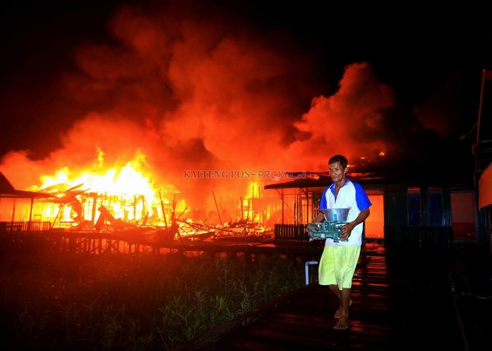 MEMBARA: Seorang warga menyelamatkan barang-barang berharga keluar rumah saat kobaran api membakar kompleks pemukiman, Minggu (25/7) pukul 02.00 WIB. DENAR/KALTENG POS